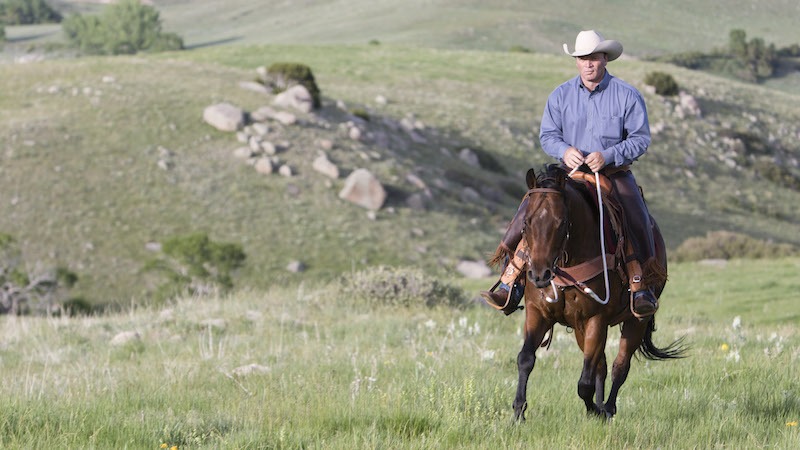 Ken McNabb riding a horse through rocky pasture