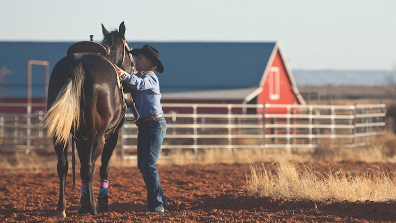 Dena Kirkpatrick adjusting saddle on horse at a ranch