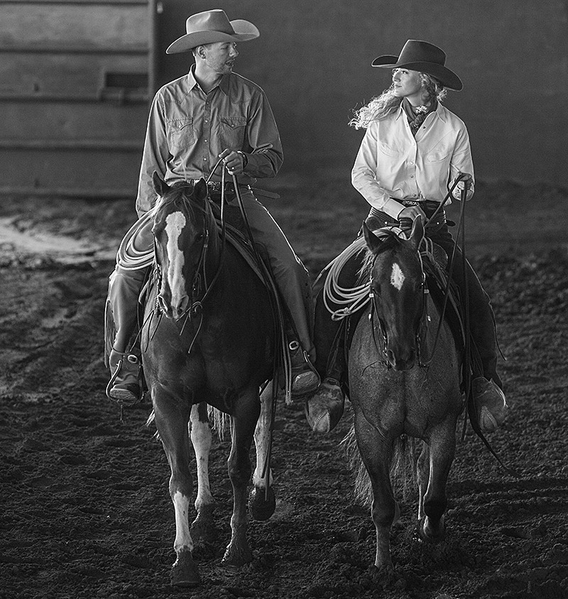 husband and wife riding horses next to each other in an arena
