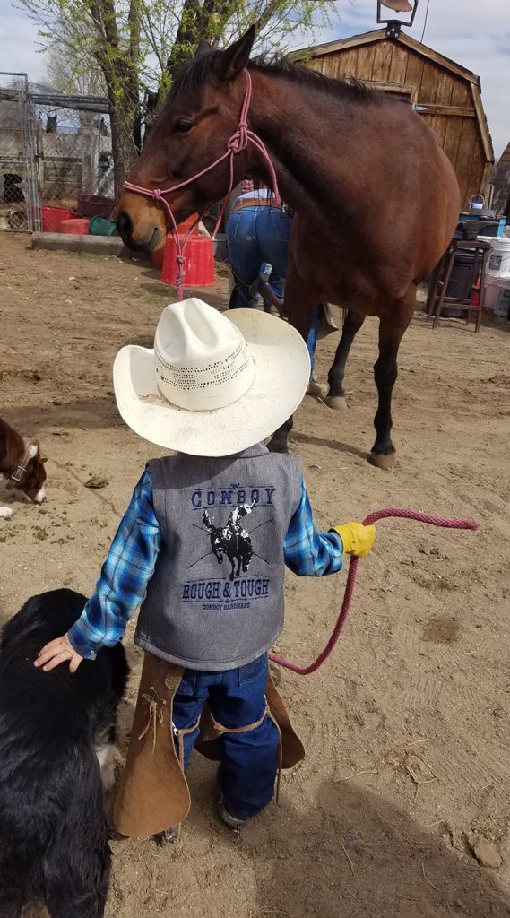 young cowboy pets dog while holding horse halter