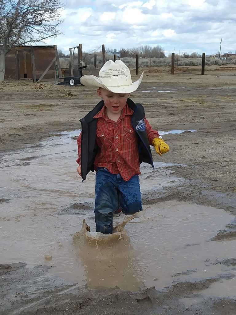 little cowboy stomps through mud puddle
