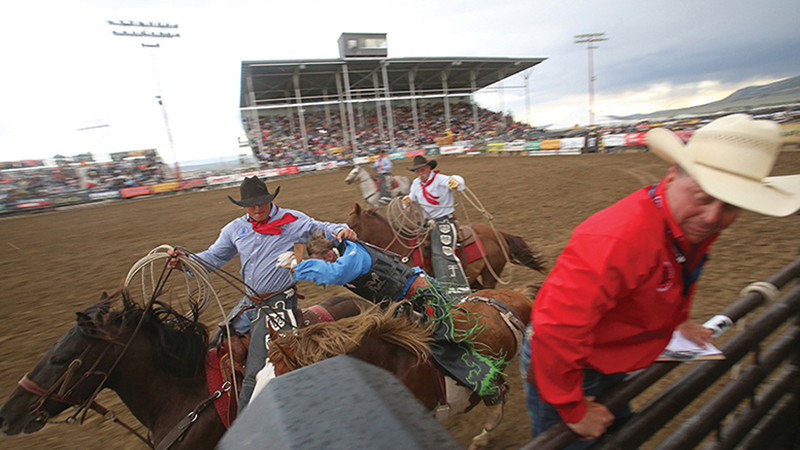 pick-up men grab bronc rider at National High School Finals Rodeo