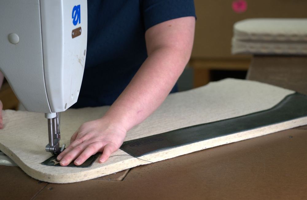 A person sews a patch onto a saddle pad.