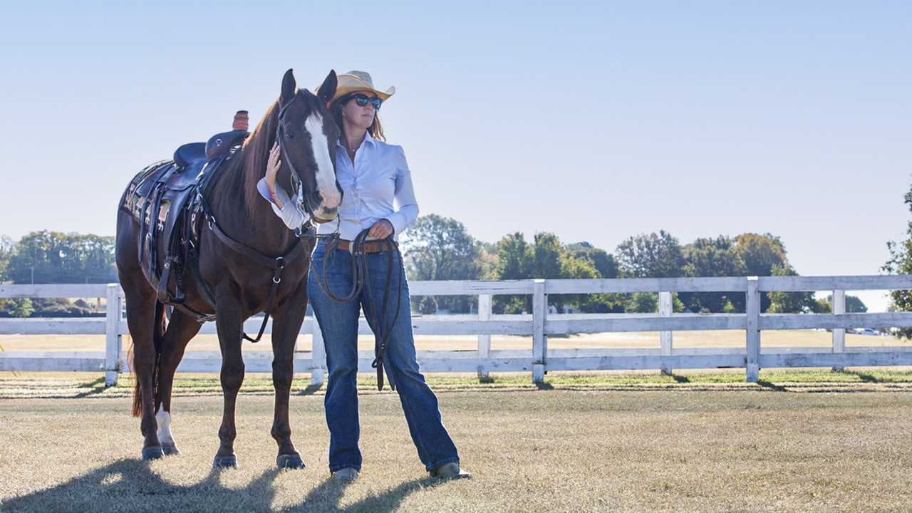 Lady standing in front of a fence with her horse.