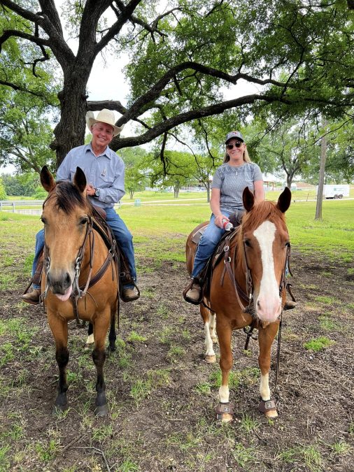 A man and women sit on top of horses.