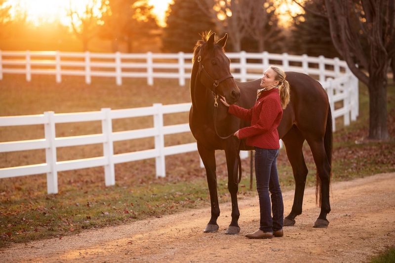 Girl standing with her horse on a pathway at sunset