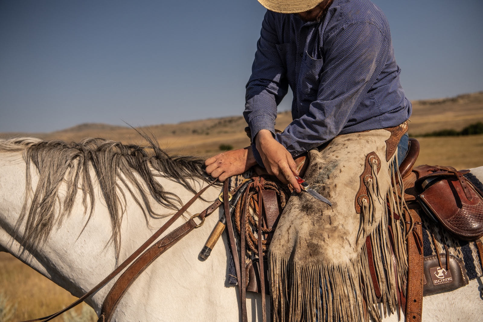 Cowboy on a horse wiping the blade of his case knife off on his chaps